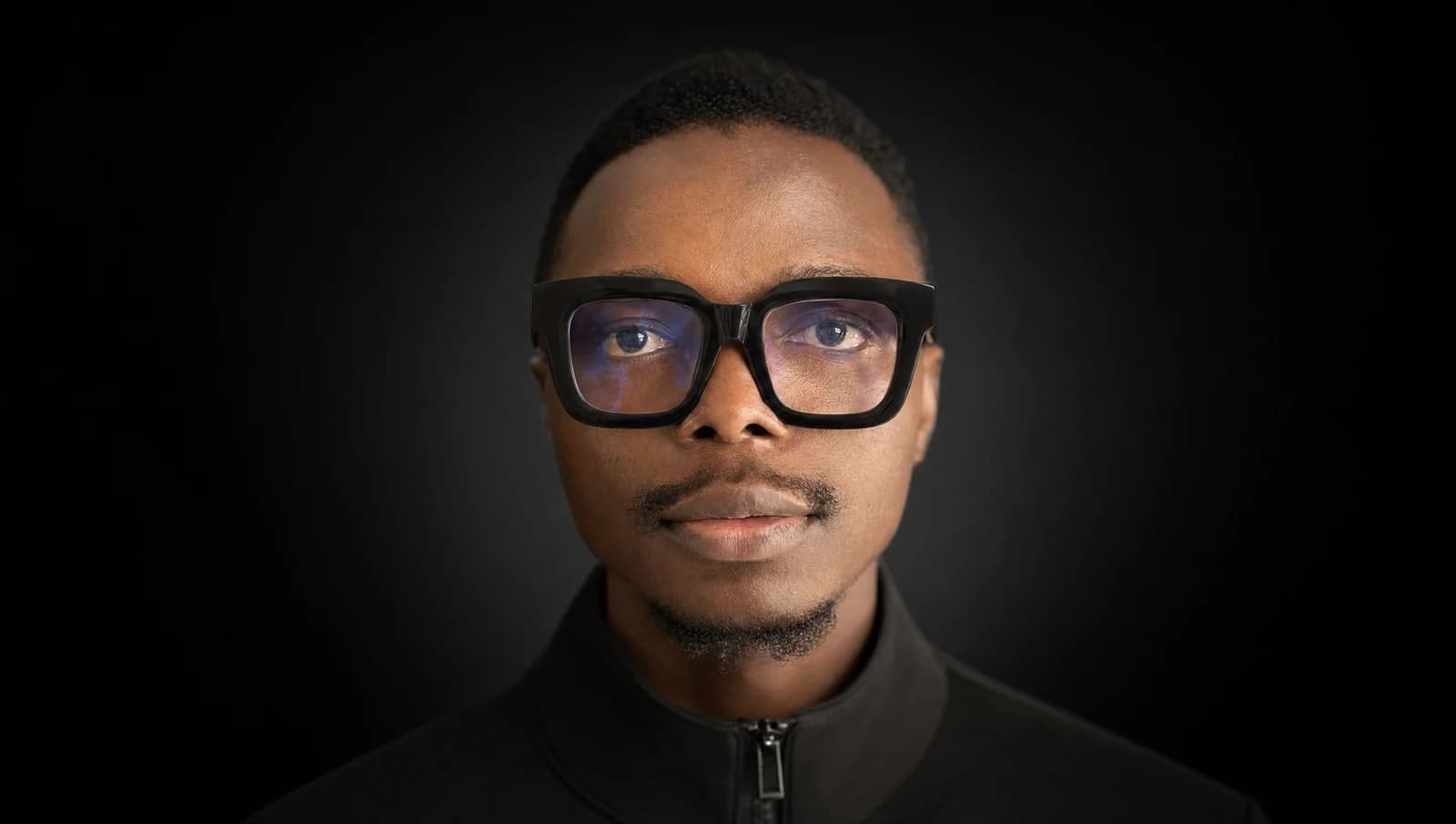 Big Quiv in a studio portrait, wearing black glasses.